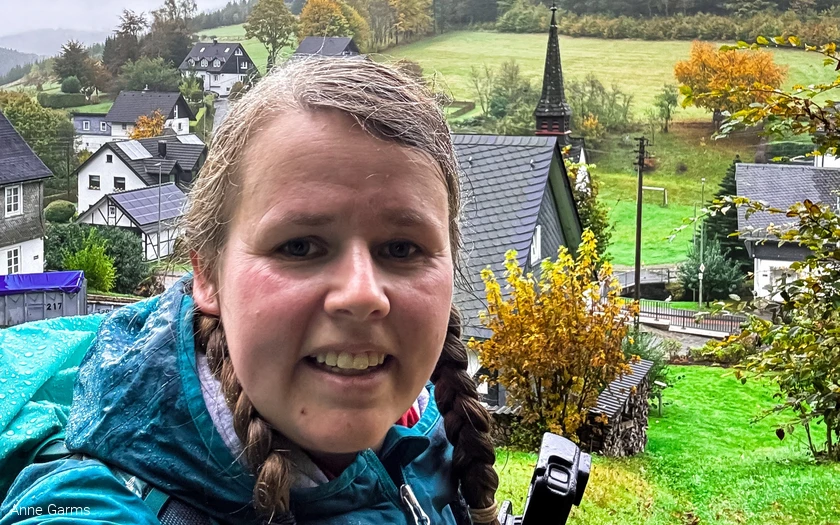 Anne macht ein Selfie im Regen. Hinter ihr befindet sich das Dorf Wirme im Tal
